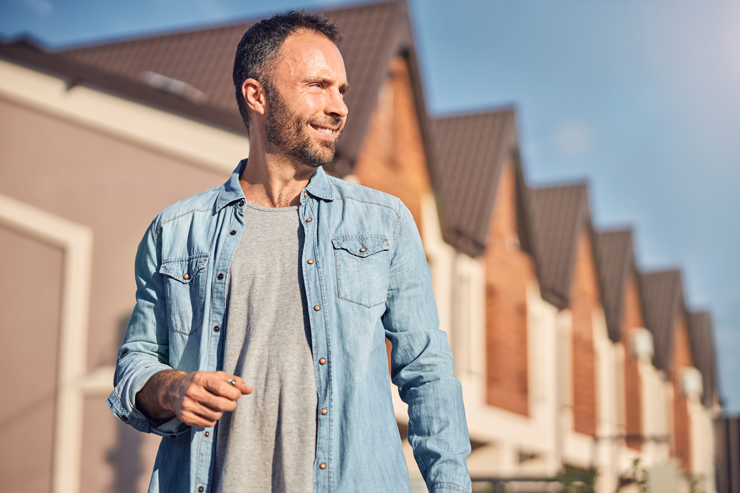 Waist-up photo of a successful young man standing in front of a newly-built house